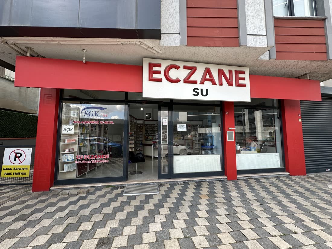 Su Eczanesi'nin Seyitgazi Sokak üzerindeki dış cephesi, kırmızı ECZANE tabelası.